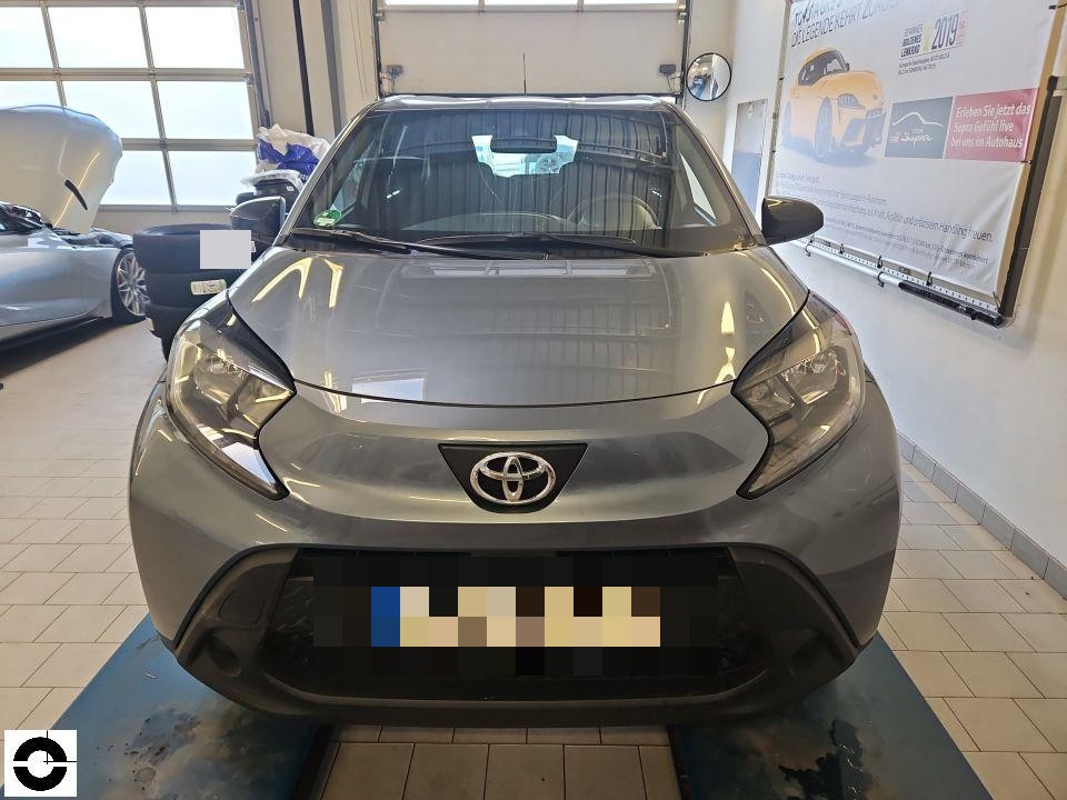 Frontansicht in Werkstatt, silbergrauer Kleinwagen, Kennzeichen pixeliert, kein sichtbarer Schaden