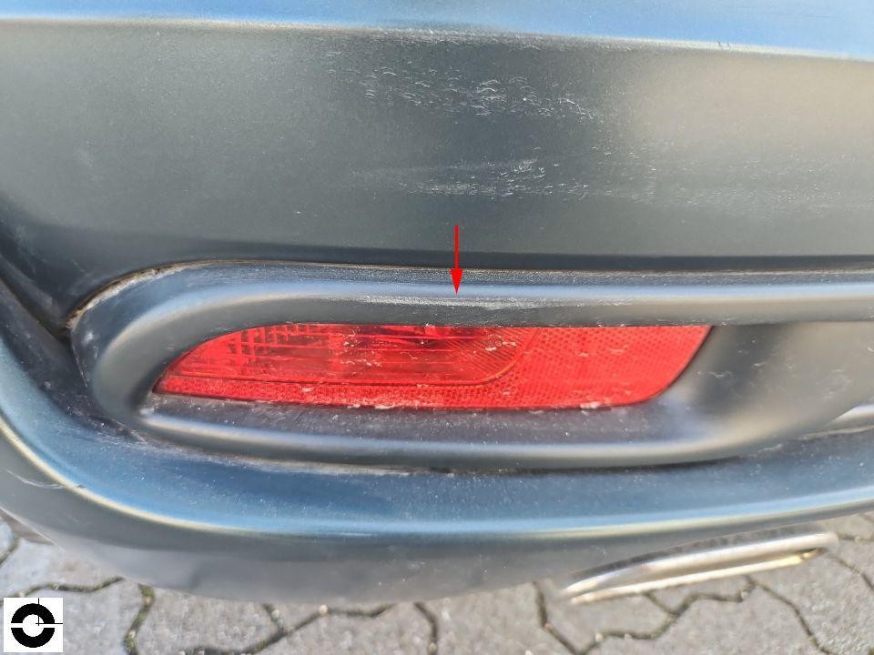 Detailaufnahme hintere Stoßstange mit Rückstrahler, roter Pfeil markiert Kratzer