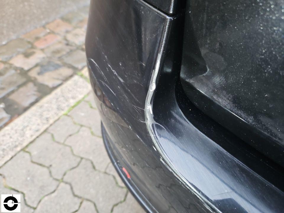 Heckbereich links, Kratzer und Lackschaden an schwarzer Stoßstange nahe Heckscheibe