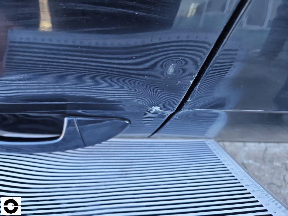 Detailaufnahme Motorhaube mit Streifenlicht-Reflexion zeigt Delle und Lackabplatzer